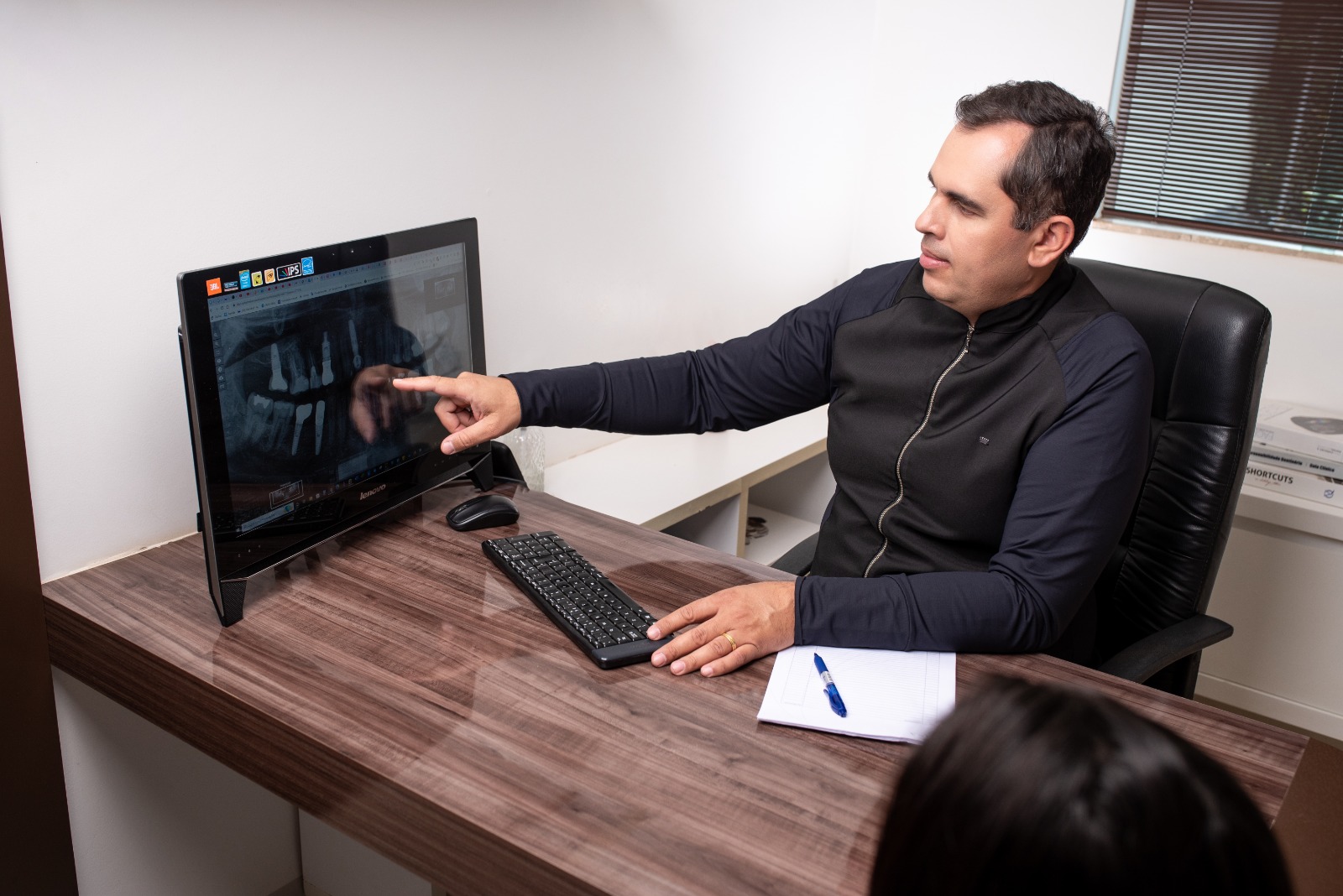 Dr. Ranieri analisando radiografia panorâmica com implantes dentários ao lado do paciente